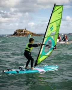 A teenage windsurfer balancing confidently on a stable school windsurf board in the bay of Piégu at Pléneuf-Val-André. Dressed in a full neoprene wetsuit and a